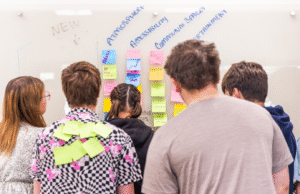 Teens stand at a whiteboard with sticky notes