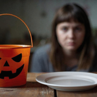 An empty Halloween bucket and plate sit on a table as a woman looks on, symbolizing hunger and food insecurity.