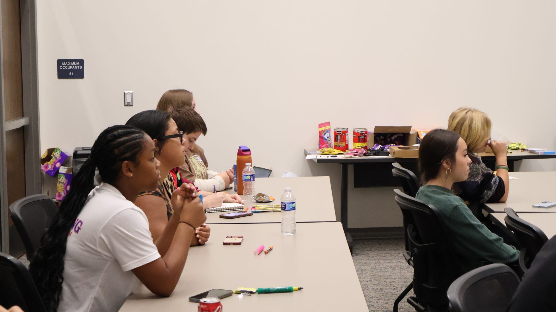 Teens sit at tables listening during the Youth Takeover Week check-in